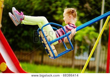 Happy little girl swinging on playground area