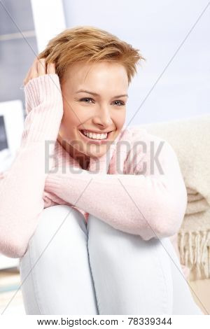 Happy woman smiling with legs pulled up, hand in hair.