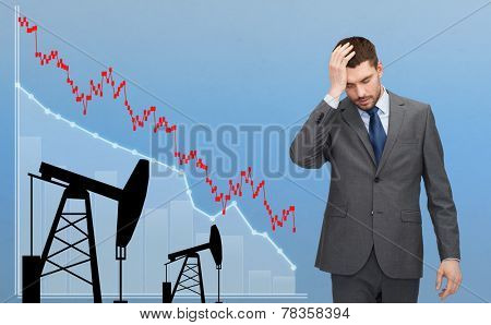 business, people, crisis, finances and economics concept - businessman with forex chart and pumpjacks touching his head over blue background