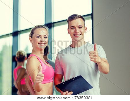fitness, sport, exercising and diet concept - smiling young woman with personal trainer in gym showing thumbs up