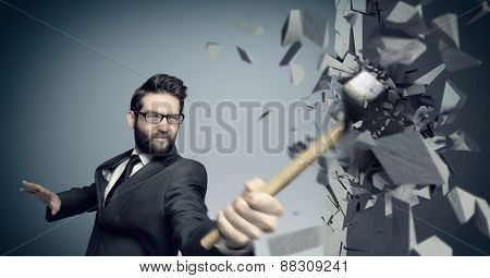 Young businessman hitting concrete wall with a hammer