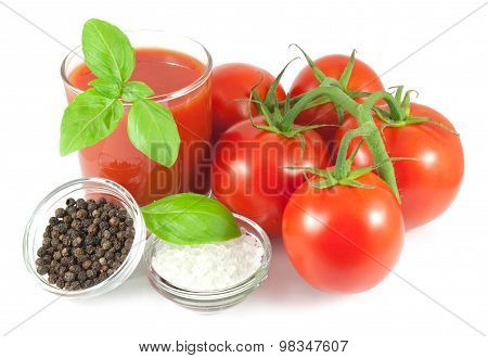 Bunch of fresh tomatoes with basil leaves, glass of tomato juice and bowls with pepper and salt