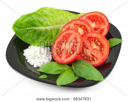 Sliced fresh tomato with basil leaves, salad leaf and sea salt on black plate isolated on white