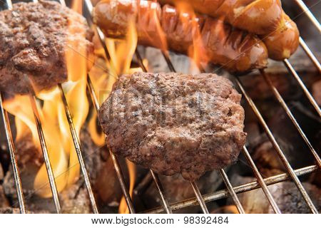 Beef Burger And Sausages Cooking Over Flames On Grill