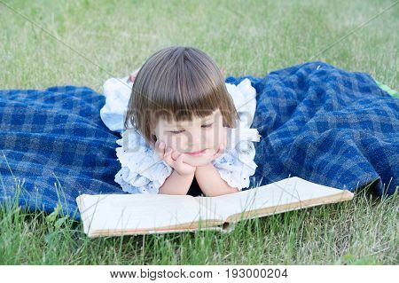 little girl reading book lying on stomach outdoor smiling cute child children education and developmen. Kids outside activity. Back to school concept