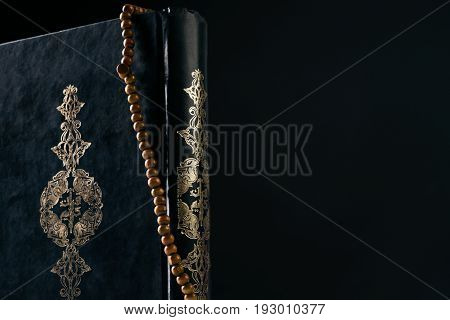 Prayer beads rosary on Koran/ Quran ( holy book of Muslims ) isolated on black background with copy space. Close-up