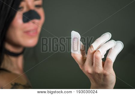 Close up of young woman wearing nails protector in her nails and a nose mask to clean skin from black spots, in a black background.