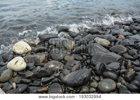 Black stones beach as a background black stones coast with silky waves from long exposure at Lipe island in Thailand.