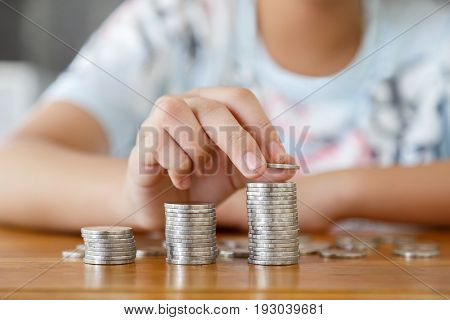 A girl putting coins to rising stack of coins on wooden table.