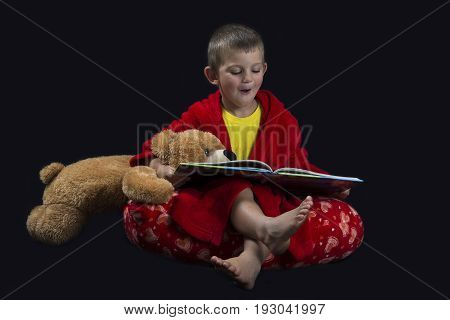 Funny boy with a teddy bear reading a book before bed time