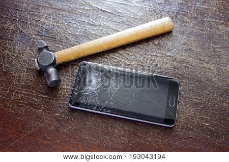 A hammer on the table near the phone with a broken screen