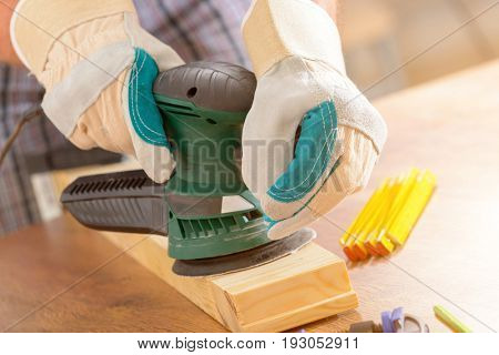 Man sanding a wood with orbital sander in a workshop