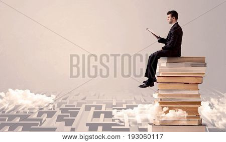 A businessman with laptop tablet in elegant suit sitting on a stack of books on top of sandy labirynth background concept