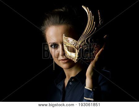 Coming out into the light. Portrait of woman in the dark dress isolated on black background holding Venetian mask