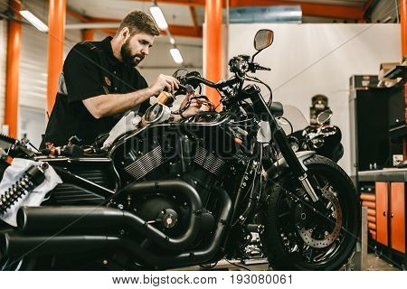 Man repairing electronics sports black bike. Confident young man repairing motorcycle in repair shop.