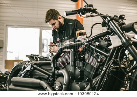 Motorcycle mechanic repairing electronics sports black bike. Handsome mechanic working in auto repair shop.