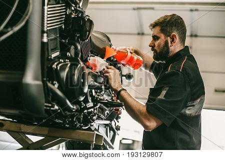Professional mechanic pouring antifreeze into a motorcycle. Confident young man repairing motorcycle in repair shop.