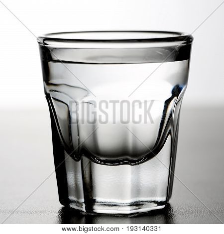 Shot glass of alcoholic drink as tequila or vodka or gin on grey gradient background