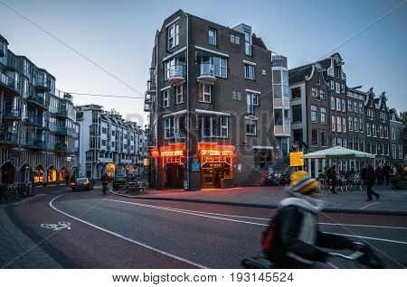 Amsterdam Netherlands - 25 April 2017: Adult rides a bicycle in historical part of Amsterdam with typical traditional houses against The Coffeeshop Reefer with legal soft drugs in evening.