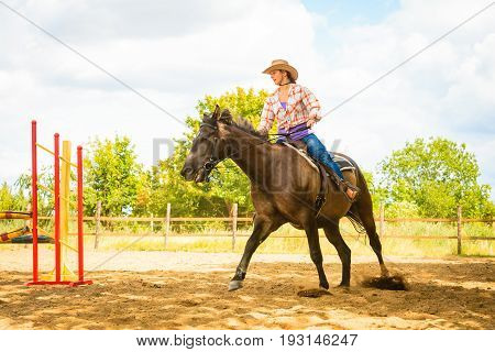 Taking care of animals horsemanship western competitions concept. Cowgirl in cowboy hat doing horse jumping through hurdle on sunny day