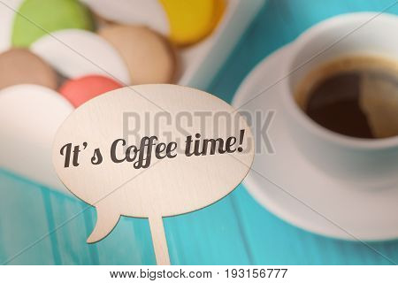 Inscription on wooden board against background of macaroons and coffee