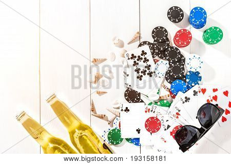 Gambling. Poker chips, cards and two bottles of beer on white wooden table. Top view. Copyspace. Poker. Summer. Sun flare