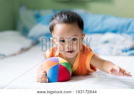 Asian adorable baby boy playing with colorful rainbow ball toy in white sunny bedroom at home.