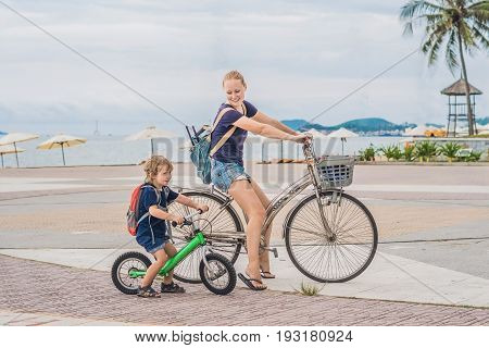 Happy Family Is Riding Bikes Outdoors And Smiling. Mom On A Bike And Son On A Balancebike