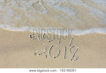 New Year 2018 text in beach sand with frothy surf water