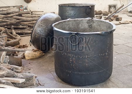 Large pans for cooking the food for pilgrims. Old pots smoked with fire in the hindu temple near the wood on the floor
