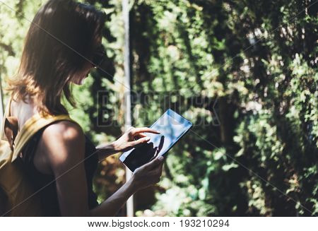 Hipster young girl with bright backpack and vintage camera using tablet or holding gadget planning travel plan. View tourist traveler on background Parc Laberint Barcelona. Mock up for text message