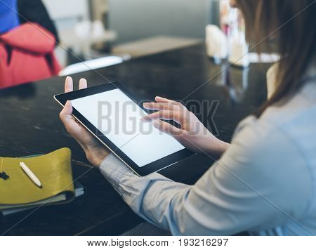 Closeup of a woman pointing finger to an blank display of the tablet with a blue color in a homelike atmosphere on warm bokeh background lighting color female hends using computer in cafe with reflection and glare