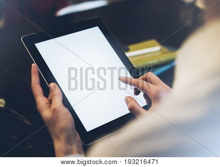 Closeup of a woman pointing finger to an blank display of the tablet with a blue color in a homelike atmosphere on warm bokeh background lighting color female hends using computer in cafe with reflection and glare