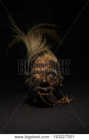 A shrunked human head from ecuador over a dark background.