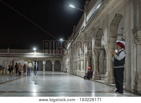 The elderly Sikh makes a prayer in the yard of the temple of Gurudwara Bangla Sahib against the background of gallery of surrounding Sarowar pond. On March 14 2017 New-Delhi India.