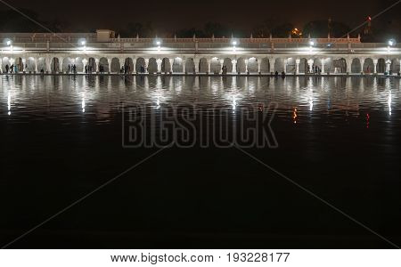 Night view of gallery of one of the main Sikh shrines - the temple of Gurudwara Bangla Sahib. The construction in night illumination is reflected in Sarowar pond water.