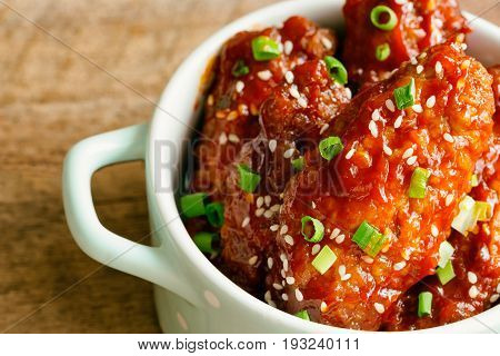 Korean fried chicken wings sprinkled with sesame and spring-onion on wood plate. Korean barbecue chicken wing delicious moist and spicy. Close up view of fried chicken wings in Korean style on wood table with copy space.