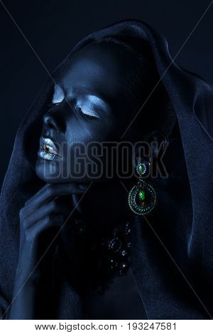 Beautiful young woman with perfect black skin and silver glitter lips wearing beautiful necklace, earrings and black veil. Cosmetics and make-up. Jewelry and bijouterie. Body painting project