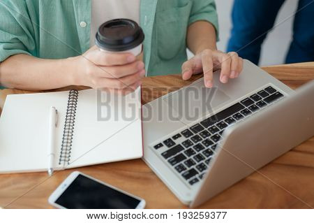 Asian hipster male with casual cloths using laptop computer touchpad while drinking coffee in cafe on workday. Freelance worker lifestyle and activity concept