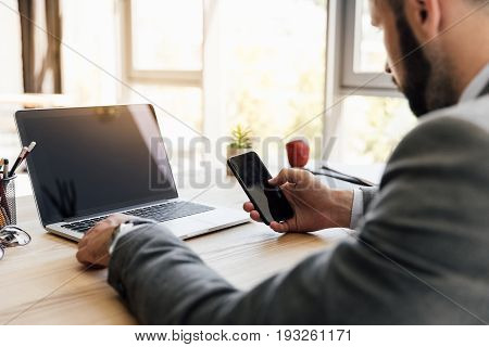 Side View Of Businessman Using Smartphone While Working On Laptop At Workplace