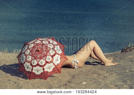 Beautiful naked female lies on the beach under a red umbrella. Girl on the sand under the umbrella