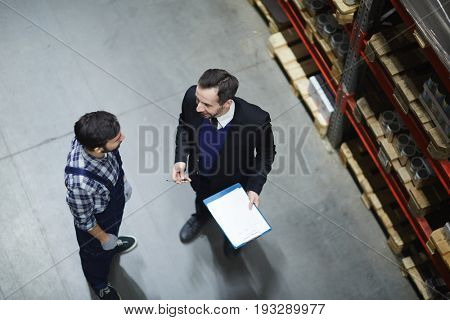 Owner of storehouse giving consignment note to worker to sign