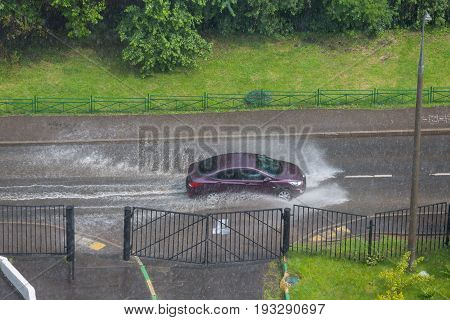 Violet car rides in heavy rain on a flooded road