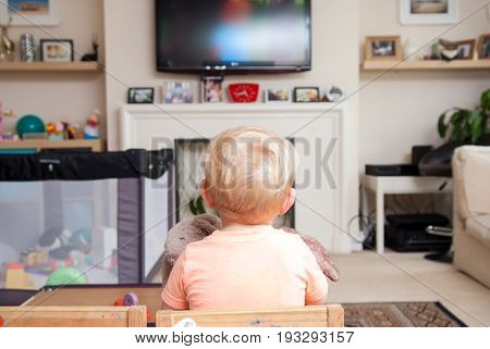 Young child at home watching televsion sitting on a small chair