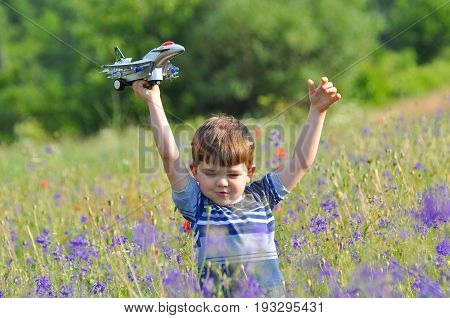 Happy boy play with airplane toy on meadow full of flowers. Little boy dreams to be a pilot one day and play with airplane