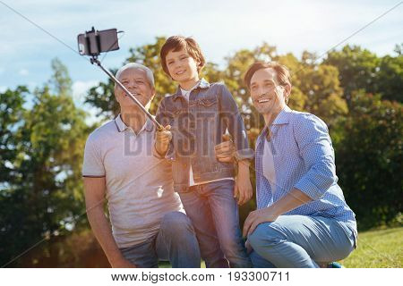Making memories. Creative happy bright relatives spending time in the park and posing for a picture while the boy taking a selfie