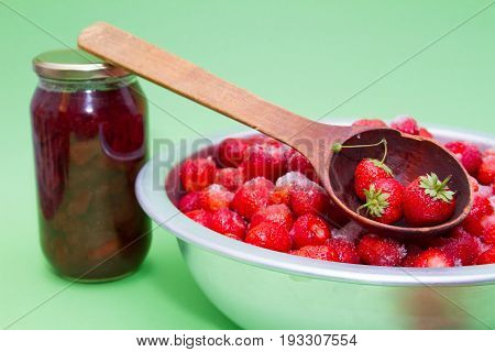 Strawberries from the manufacturer with sugar and jars for making jam on a green background.