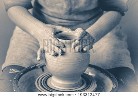 Photo in old vintage style. Girl sculpts in clay pot closeup. Modeling clay close-up. Caucasian man making vessel daytime of white clay in fast moving circle.
