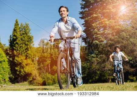 Catch me. Original productive motived gentleman engaging his son in sporty activities while taking a ride on a bicycle and enjoying the day outdoors
