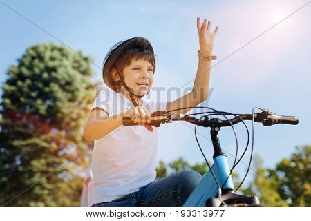 Hey there. Bright incredible sincere child spotting his friend and greeting him while meeting for a bike ride together